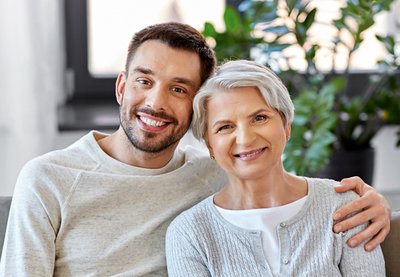 Ein jüngerer Mann legt den Arm um eine ältere Frau, beide lächeln in die Kamera