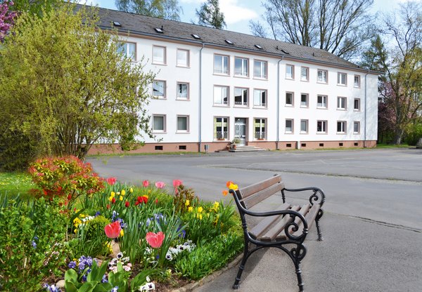 Haus Benedikt am zentralen Parkplatz, im Vordergrund Blumen und eine Bank